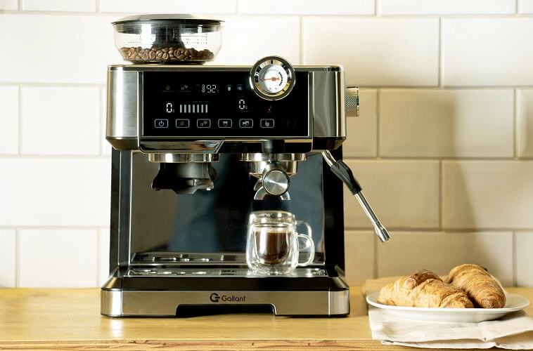 Imagem da Cafeteira em uma superfície de madeira ao lado de um prato com croissants