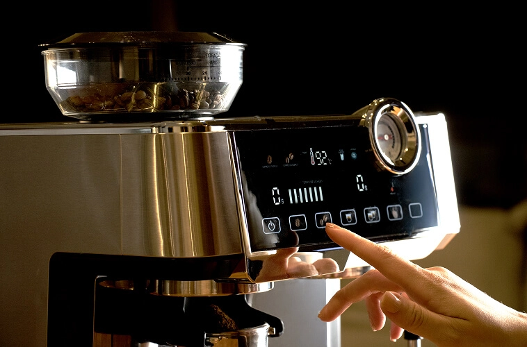 Imagem de uma mão se aproximando da cafeteira para utilizá-la